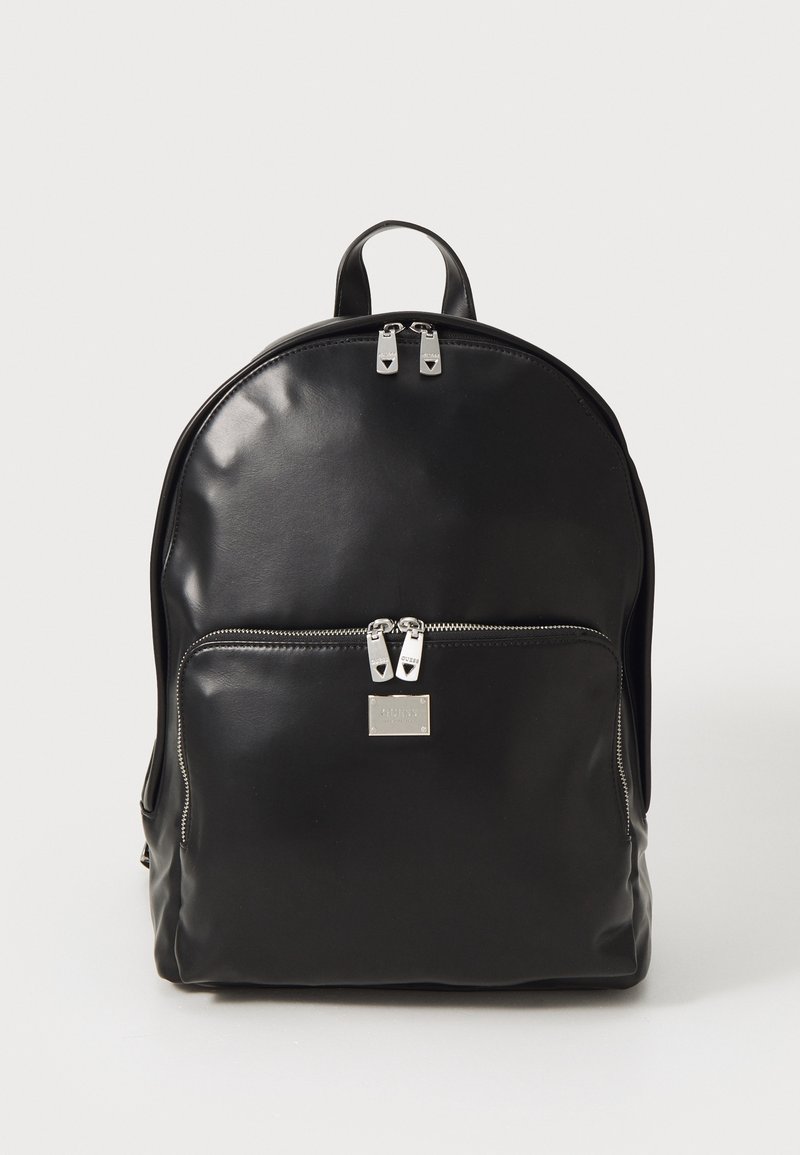 Zwarte leren rugzak met een gestructureerde vorm, voorzien van een voorvak, zilverkleurige ritsen en een metalen merkteken. Glad oppervlak.