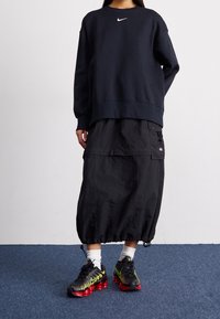 Navy sweatshirt with white Nike logo, black cargo skirt with adjustable hem, and black sneakers with red sole and green accents.