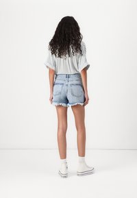 Jeansshorts med fransad fåll, ljusblå färg, kombinerat med en randig kortärmad skjorta. Modellen bär vita högstövlade sneakers.