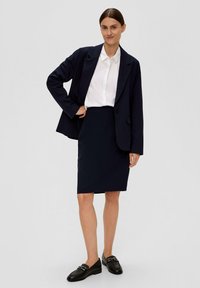 Marineblazer über einem weißen Hemd, kombiniert mit einem knielangen marineblauen Rock und schwarzen Loafers. Der Blazer hat einen einzelnen Knopf und einen Reverskragen.