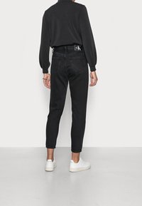 Černé džíny s vysokým pasem a rovnými nohavicemi, zadní kapsy a jemné detaily šití. Spárováno s bílými teniskami na hladkém povrchu.