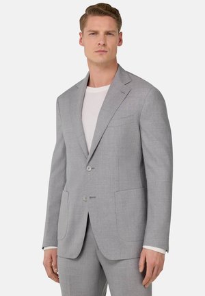 Blazer gris de tela texturizada, con dos botones, solapas de muesca y dos bolsillos frontales. Llevado sobre una camiseta blanca.