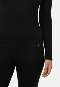 Maglietta a maniche lunghe nera con un design aderente, realizzata in tessuto testurizzato. Presenta un piccolo etichetta colorata sull'orlo.