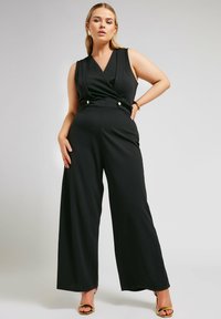 Svart ärmlös jumpsuit med en omslagstopp, vida ben och guldtonade knappdetaljer vid midjan för en skräddarsydd look.