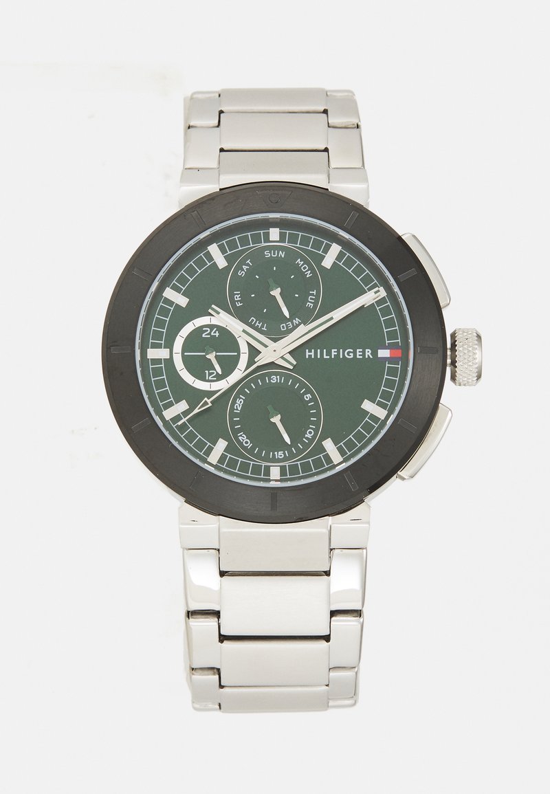 HILFIGER watch with a green analog dial, silver stainless steel band, black bezel, sub-dials for day and date, and a textured crown.