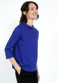 Kobaltkék felső, cseppnyakú, háromnegyedujjú és laza szabású. Puha tapintású, fekete nadrággal párosítva.