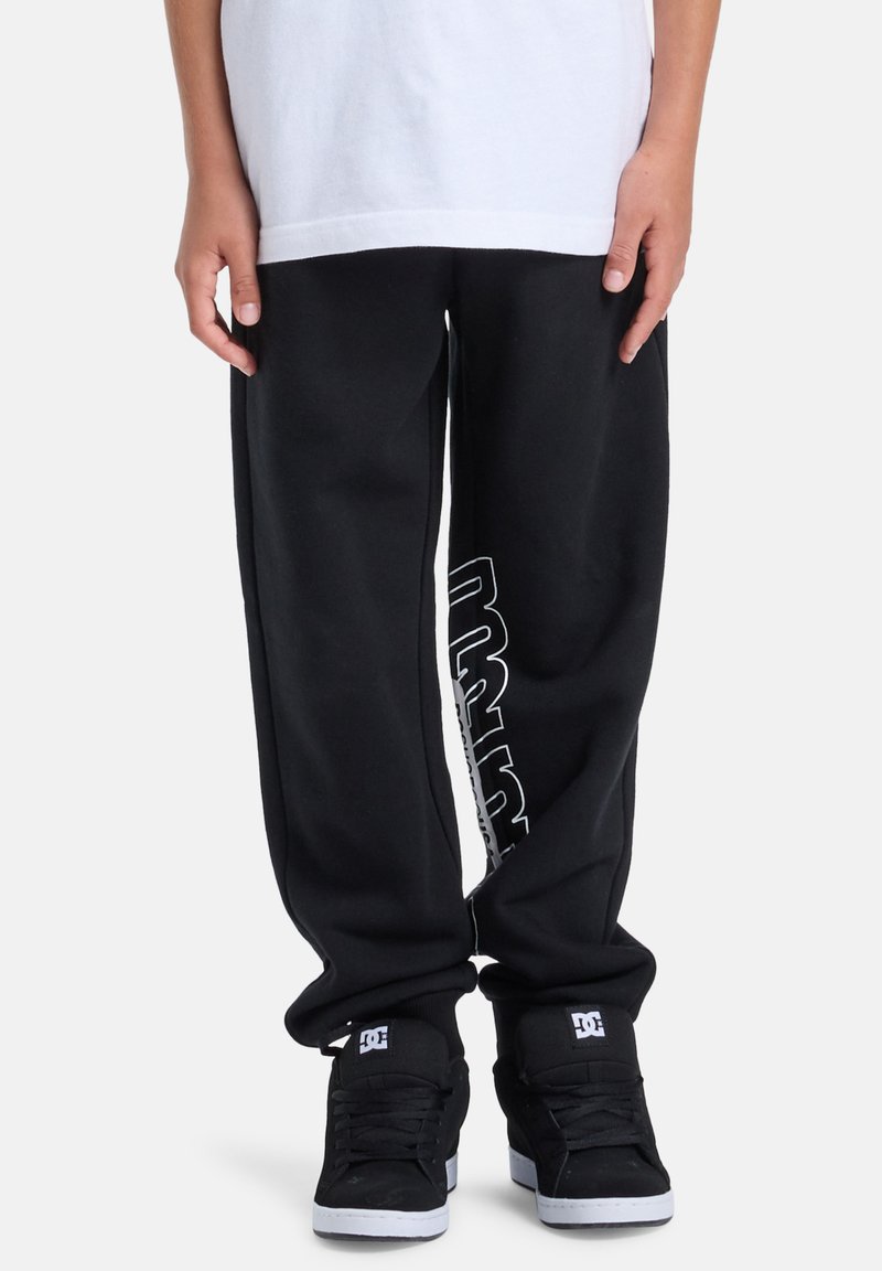 Sorte joggingbukser med en afslappet pasform, med hvidt logo langs siden. Kombineret med sorte høje sneakers og en hvid t-shirt.