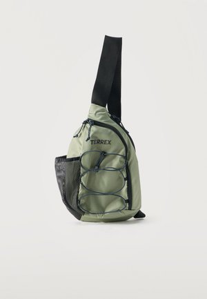 Lysegrøn Terrex slynge rygsæk med sort justerbar strop, elastiske snore foran, lynlåslommer og netlomme på siden.