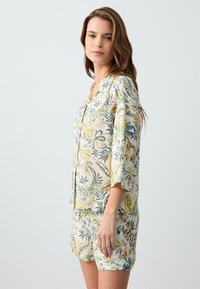 Zestaw odzieży loungewear w kwiatowy wzór z lekkiego materiału, składający się z koszuli z krótkim rękawem na guziki i pasujących szortów o luźnym kroju oraz żywych kolorach.