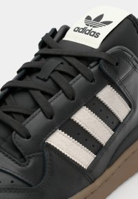 Crne kožne tene s tri bijele pruge, teksturiranim detaljima, crnim vezicama i bijelom brendiranoj jezičkoj s adidas logom.