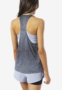 Grå sporttopp med racerback-design, i ett texturerat material. Bärs över en ljuslila sport-bh, kompletterad med blå shorts.