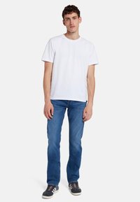 T-shirt bianco a maniche corte abbinato a jeans blu medio e sneakers scure. La maglietta presenta un collo rotondo e una vestibilità comoda.