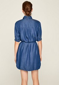 Jeansklänning i medelblått, med krage, korta uppvikta ärmar, midjeband och en rundad nederkant i knälängd.