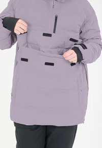 Lavendel puffy jakke med store forlommer og sorte detaljer. Har en lynlåslomme på brystet og elastiske manchetter for varme.