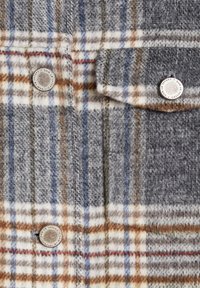 Tela de franela a cuadros en gris y marrón con líneas blancas y azules. Presenta botones plateados y una superficie texturizada, ideal para prendas exteriores.