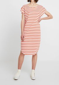Sukienka midi w poziome pomarańczowe i białe paski, z okrągłym dekoltem i krótkimi rękawami. Połączona z białymi trampkami na sznurówki.