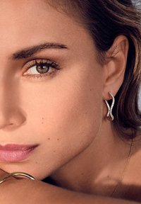 Orecchini curvi in metallo, caratterizzati da un design attorcigliato con piccoli gemme trasparenti. La superficie è liscia e lucida, riflettendo la luce.