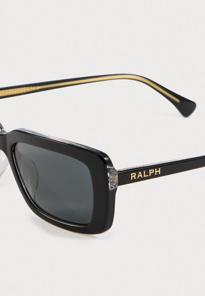 Crne pravokutne sunčane naočale s tamnim lećama i zlatnim "RALPH" logotipom na ramu, prikazane na čisto bijeloj pozadini.