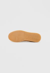 Rubber shoe sole in tan with a textured zigzag pattern and a circular logo at the center. Smooth edges and a curved design.