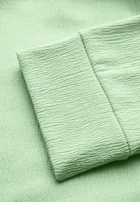 Tekstuuri, vaaleanvihreä kangas, jossa on uritettu kuvio, sisältäen taitetun osion, joka korostaa epätasaista pinnan yksityiskohtaa.