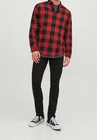 Camicia di flanella a quadri rossi e neri con maniche lunghe, chiusura con bottoni, e jeans neri. Completata con classiche sneakers bianche e nere.