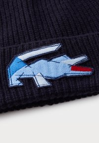 Gorro de malha azul-marinho com um logótipo bordado multicolorido, tendo tons de azul claro, azul escuro e vermelho. Tecido texturizado para aquecimento.