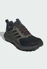 Schwarzer und olivfarbener Laufschuh mit einer strukturierten Oberseite, drei schwarzen Streifen, orangefarbenen Schnüren und einer robusten Sohle. Mit CLIMAPROOF-Branding.