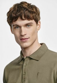 Oliwkowa koszulka polo wykonana z bawełny, z klasycznym kołnierzykiem, trzema guzikami i małym haftowanym logo na piersi.