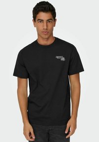 Camiseta de algodón negra con mangas cortas, cuello redondo y un diseño frontal que presenta el texto "Spaghetti Bolognese" en un color contrastante.