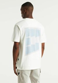 T-shirt bianca in cotone con un motivo a griglia blu sul retro, maniche corte e scollatura rotonda, con spacchi laterali.