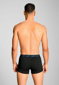 Black boxer briefs with a blue Puma logo on the elastic waistband, worn by a person facing away, showcasing a fitted design and smooth texture.