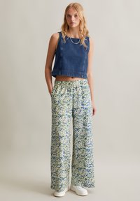 Denim crop top with square neckline paired with wide-leg floral print pants in green, blue, and white. Model wearing white sneakers.