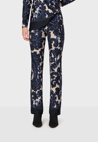 Byxor med blommönster i marinblått och beige. Mjuk tyg med en figurnära design, med en svart mudd vid fållen. Bärs med svarta ankelstövlar.