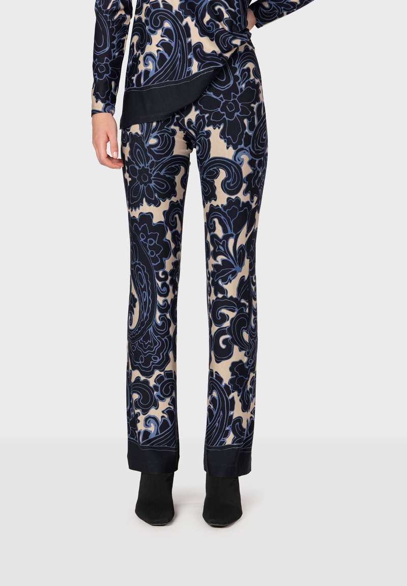 Byxor med blommönster i marinblått och beige. Mjuk tyg med en figurnära design, med en svart mudd vid fållen. Bärs med svarta ankelstövlar.