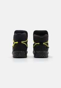 Zapatillas altas negras con parte superior de tejido texturizado, cordones amarillos y suela negra moteada. Diseñadas con soporte acolchado para el tobillo.