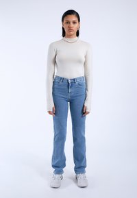 Light beige long-sleeve top paired with high-waisted blue jeans, fitted through the hips, and white athletic shoes. Simple design, no patterns.