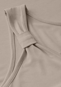 Beige ärmlös topp med en vriden detalj vid axeln. Tyget är slätt med en subtil textur och mjuka kanter.