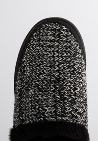 Zwart en grijs gebreide instapschoen met een gestructureerde bovenkant, zachte zwarte bontvoering en een platte rubberen zool.