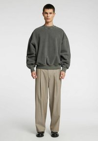 Felpa grigia oversize con spalle scese, polsini e orlo a costine, abbinata a pantaloni beige a gamba larga e scarpe nere.