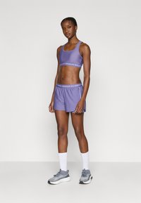 Μωβ αθλητική κοντή μπλούζα και σορτς, με ελαστική μέση με λογότυπο. Το μοντέλο φοράει γκρι αθλητικά παπούτσια και λευκές κάλτσες. Ομαλή υφή, εφαρμοστή σχεδίαση.