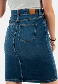 Jupe en denim bleu foncé avec taille haute, cinq poches et patch en cuir de la marque. Présente une coupe droite et une légère texture.