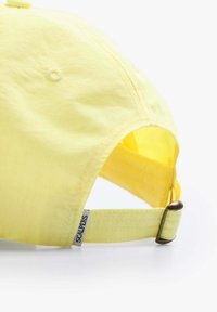 Yellow fabric baseball cap with a curved peak, adjustable strap, and a logo tag on the side. Soft texture and simple design.