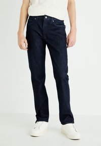 Dark blue denim jeans with a straight leg design, featuring a five-pocket style and metal button closure, paired with white sneakers.