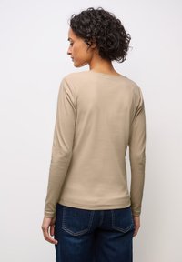 Beige Langarm-Oberteil mit Rippstruktur und Rundhalsausschnitt, kombiniert mit dunkelblauen Jeans. Der Stoff hat eine strukturierte Optik und eine figurbetonte Passform.