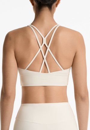 Soutien-gorge de sport beige clair avec un design de bretelles croisées au dos, texture lisse et branding subtil près de l'ourlet.