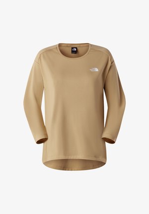 Beżowa koszula z długim rękawem i okrągłym dekoltem, wykonana z gładkiej tkaniny. Na lewej górnej części piersi znajduje się białe logo The North Face.