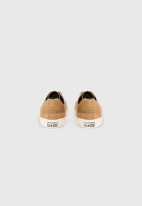 Brązowe skórzane sneakersy o niskim profilu, z teksturowanym wykończeniem i białymi gumowymi podeszwami. Logo "Converse All Star" na pięcie.