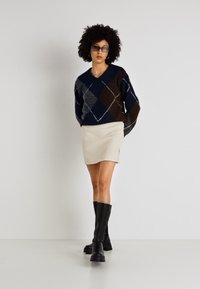 Sweter dzianinowy w wzór argyle w granatowym, brązowym i szarym kolorze, z dekoltem w kształcie litery V, zestawiony z kremową spódnicą z sztruksu i czarnymi kozakami za kolano.