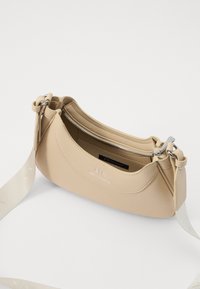 Borsa a tracolla in pelle beige con finitura testurizzata, forma curva, accessori in argento e tracolla removibile con dettagli del logo. Scomparto principale con zip.