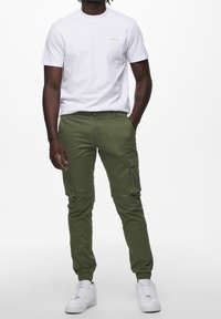 Vit t-shirt med kort ärm och tryck av "CAMEL UP"; tillsammans med gröna cargobyxor med sidfickor och elastiska mudd. Vita sneakers.